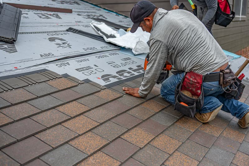 Roofer kneeling on a shingle roof over new underlayment